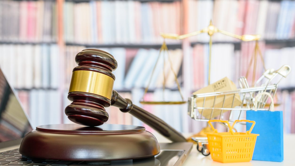 Consumer rights and consumer protection, business law concept : Judge gavel on a laptop computer with shopping basket, shopping bags and a shopping cart, balance sale of justice and bookshelf behind.