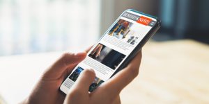 Businessman hand holding black smartphone with reading online news on website on desk in the office.