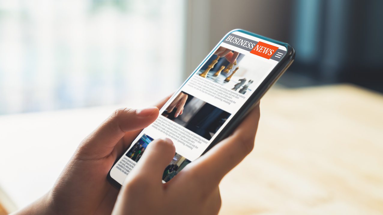 Businessman hand holding black smartphone with reading online news on website on desk in the office.