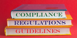 Books with words compliance, regulations and guidelines on red background.