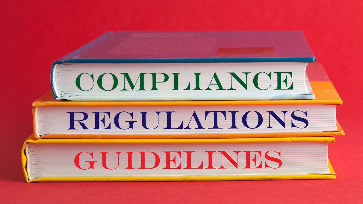 Books with words compliance, regulations and guidelines on red background.