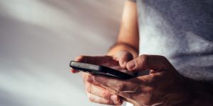 Man using modern smartphone portable information device to type text message, selective focus