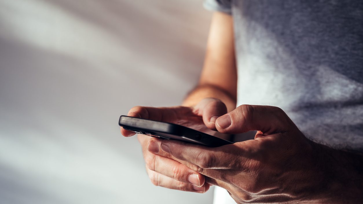 Man using modern smartphone portable information device to type text message, selective focus