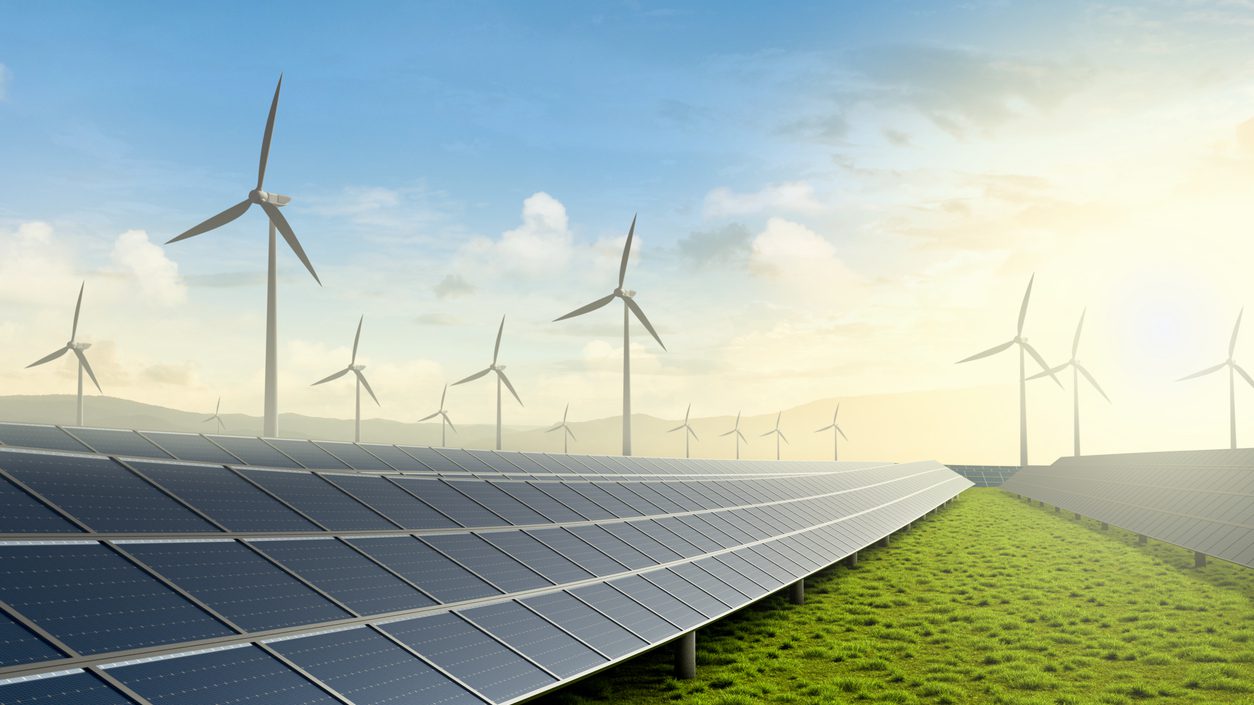 Solar farm and wind turbine on green fields with beautiful sunset