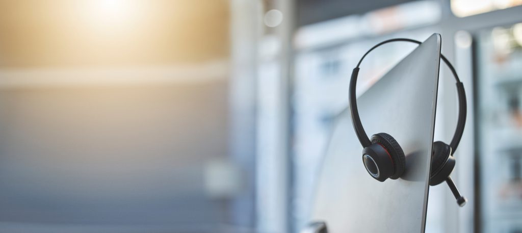 Call center, headset on a computer in an empty office with flare and mockup for communication or assistance. Customer care, support and equipment in a workplace after hours for help or service